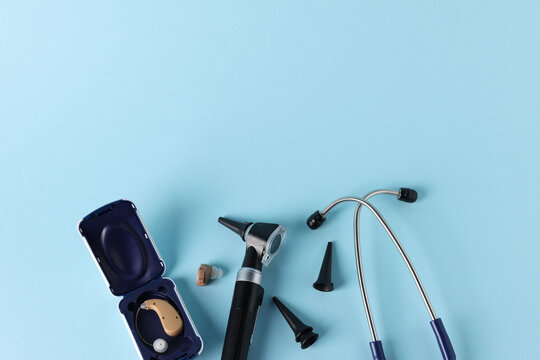 Modern otoscope, hearing aid, stethoscope and ear speculums on light blue background, flat lay. Space for text