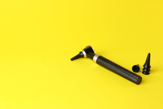 Hearing test. Modern otoscope and ear speculums on yellow background, closeup. Space for text
