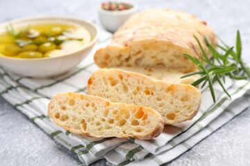 Fresh cut ciabatta, oil, olives and rosemary on grey textured table, closeup
