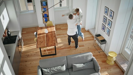 Joyful couple spinning indoors top view. Excited woman jumping meeting boyfriend
