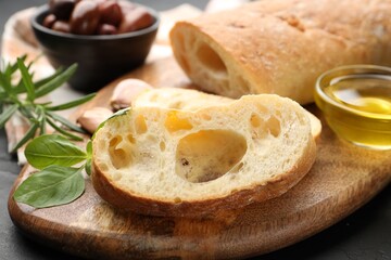 Fresh cut ciabatta, oil, rosemary and basil on dark textured table, closeup