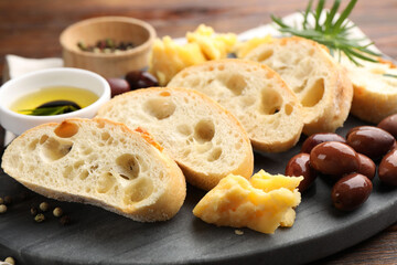 Pieces of fresh ciabatta, oil, olives, cheese and peppercorns on wooden table, closeup