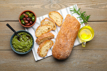 Cut ciabatta, spices and olives on wooden table, flat lay