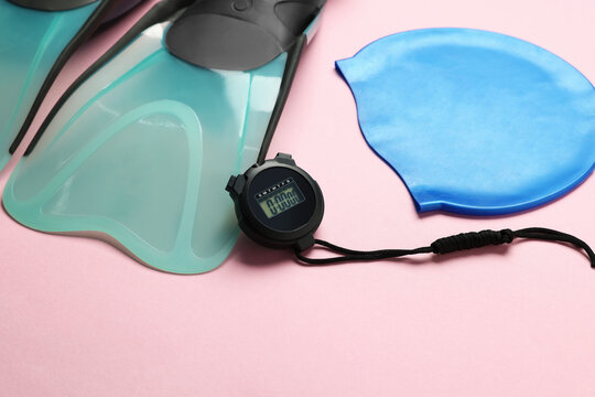 Flippers, digital stopwatch and swim cap on pink background, closeup
