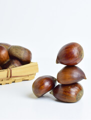 Chestnuts stacked and in a basket on a white background. Close up and vertical.