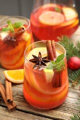 Tasty punch drink in glasses, spices, jug and Christmas decor on wooden table, closeup