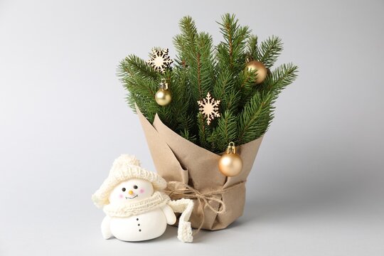 Beautiful Christmas tree branches with baubles, wooden snowflakes wrapped in paper and decorative snowman on grey background, closeup