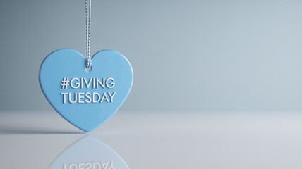 #GIVINGTUESDAY text on a smooth blue heart tag hanging from a string, reflected on a shiny white surface against a minimalist clean background for charity promotion Giving Tuesday
