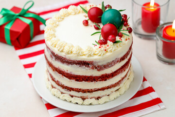 Delicious sponge cake with Christmas decor, gift box and burning candles on light table, closeup