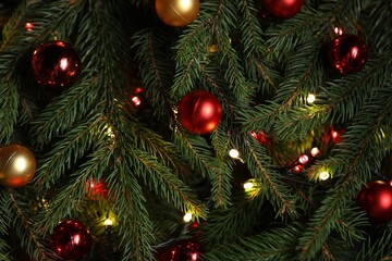 Beautiful spruce tree branches with Christmas ornaments and lights as background, top view