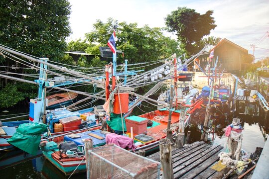 Traditional Thai fishing boats moored at a local pier in a coastal village. Authentic fisherman lifestyle featuring colorful wooden boats, fishing nets, and equipment under bright daylight. Scenic nau