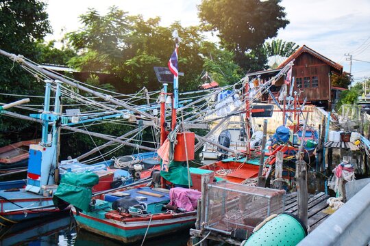 Traditional Thai fishing boats moored at a local pier in a coastal village. Authentic fisherman lifestyle featuring colorful wooden boats, fishing nets, and equipment under bright daylight. Scenic nau