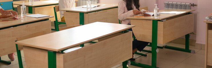 Several students sitting at separate desks during classroom activity, banner. Education, distance learning, and modern safety in academic environment.