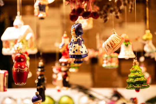 March&eacute; de No&euml;l en Alsace, d&eacute;corations suspendues sur un stand, boules en forme de personnages et objets traditionnels, &eacute;clairage chaleureux 