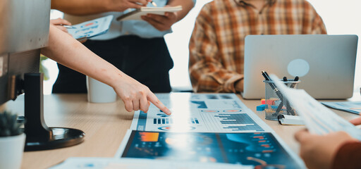 A group of professionals engages in a collaborative meeting, analyzing data charts and discussing insights in a contemporary workspace filled with technology and documents. SACTR