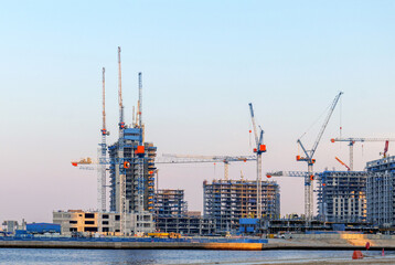 Modern construction site with multiple cranes and high-rise buildings rising by the sea. Dynamic view of urban development, progress, and construction in Dubai