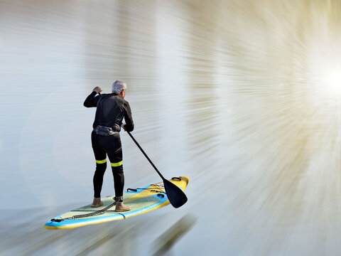 An elderly man swims in the water on a sport tourist inflatable spray with a paddle. Artistic blur speed. Activity of people in old age. Modern water sports. Surfing with a paddle. Water activities