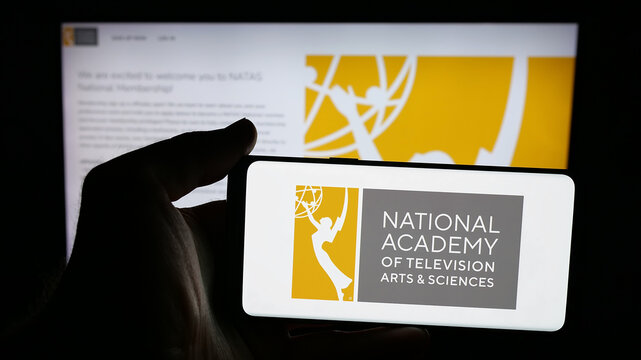 Stuttgart, Germany - 10-31-2025: Person holding mobile phone with logo of US television award Emmy Awards (Emmys) on screen in front of web page. Focus on phone display.