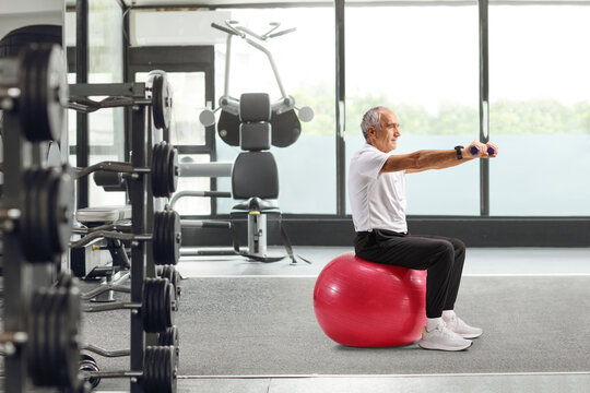 Mature man exercising with dumbbells seated on a fitness ball - Powered by Adobe