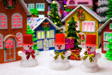 Three snowmen in red hats in front of a Christmas town