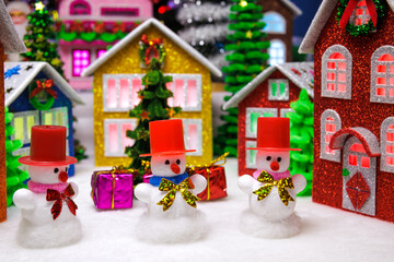 Three snowmen in red hats among the houses of a Christmas town