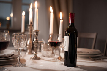 Elegant dinner table set with glowing candlelight, red wine bottle, crystal glasses, plates, romantic ambiance, festive celebration, cozy home dining, luxurious atmosphere, fine dining
