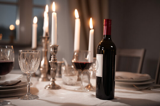 Elegant dinner table set with glowing candlelight, red wine bottle, crystal glasses, plates, romantic ambiance, festive celebration, cozy home dining, luxurious atmosphere, fine dining
