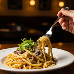 Closeup of a hand holding a fork with spaghetti carbonara, garnished with fresh herbs and parmesan cheese