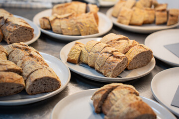 Multiple plates displaying freshly sliced rustic artisan bread loaves, each piece dusted with a light flour coating, arranged on a metallic counter.
