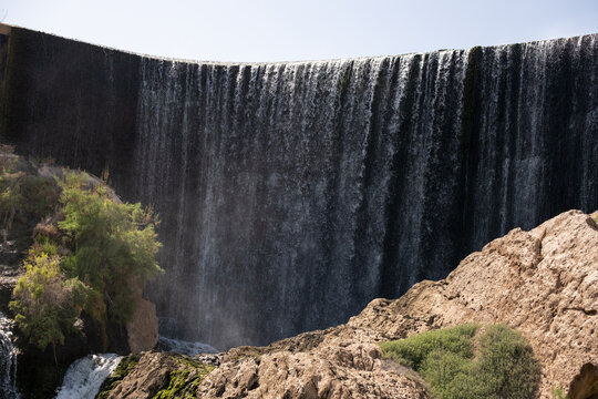 Majestic waterfall cascading over rocky cliff with lush greenery in sunlight