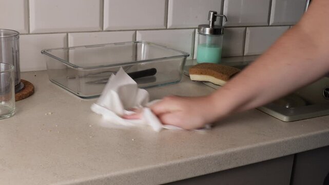 Hand cleaning a smooth kitchen countertop with a soft cloth, removing dust and stains as part of regular home hygiene and maintenance