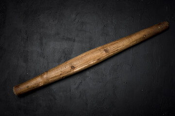 Used, rustic wooden rolling pin on dark, textured black background