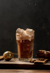 A glass of hot chocolate or cocoa with lots of cinnamon-dusted marshmallows on a dark background. A cozy winter drink.