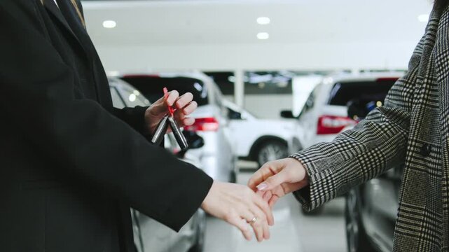 Saleswoman gives to client a car keys after complete car purchase with handshake at automobile dealership during a test drive consultation