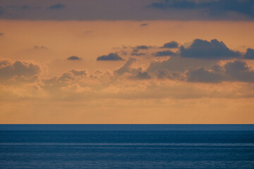 Obraz premium A serene seascape captures a warm sunset spilling pink and orange hues across the sky while the blue ocean stretches to the horizon, inviting calm, reflection, and quiet contemplation.