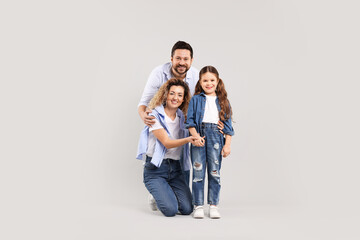 Fototapeta premium Happy parents and their daughter hugging on grey background. Family bonding