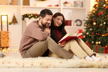 Obraz premium Happy couple reading book together in room decorated for Christmas