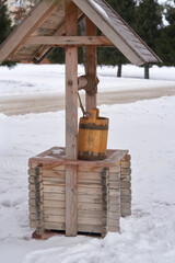 A wooden well under a roof with a wooden bucket on a rope. Vintage. Winter snowy landscape. © ROMAN DZIUBALO