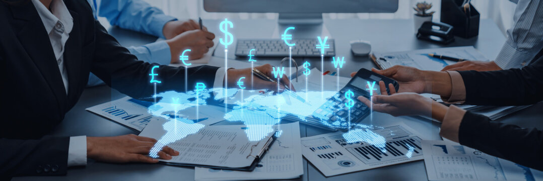 Diverse professionals engage in a business meeting, discussing financial strategies while utilizing technology and currency symbols for global trading insights. Trope - Powered by Adobe