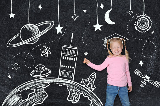 Cute little child near black chalkboard with drawings. Girl imagine herself as graduate student
