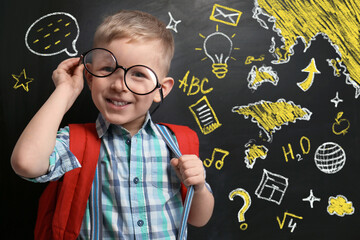 Cute little child in glasses near black chalkboard with drawings