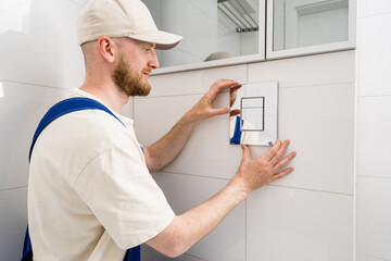 Repairman installs flush button for concealed cistern in modern bathroom setup