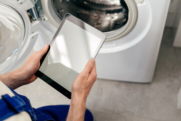 Repairman uses tablet for maintenance of washing machine in home laundry room