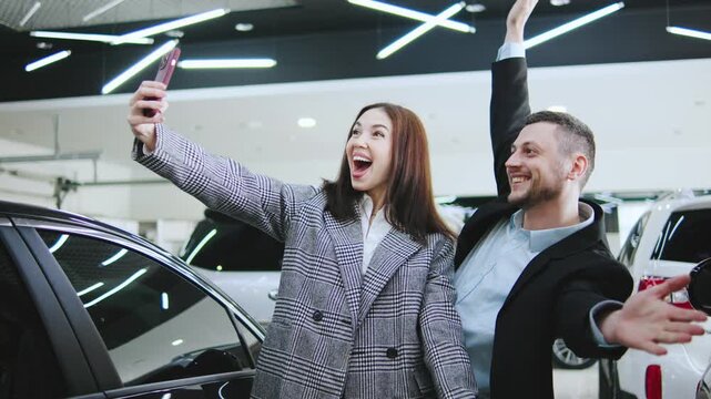 Happy couple joyfully poses for a selfie after completing a car purchase at the dealership. The atmosphere is vibrant and celebratory.