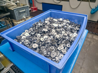 Metal pieces await next processing stage in the blue plastic box inside a manufacturing plant