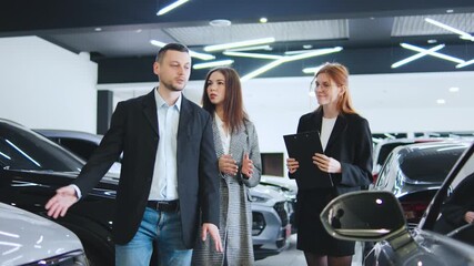 Saleswoman guides clients happy couple through car options at an automobile dealership, discussing features and setting up test drives to close a deal successfully.
