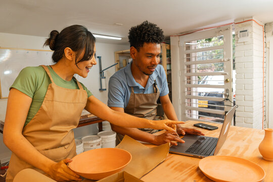 Latin American entrepreneurs managing online pottery business with laptop