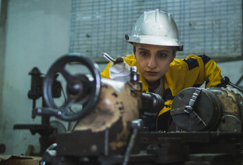 technician woman wearing safety helmet and yellow jacket is working with a lathe machine in an industrial factory. The image highlights dedication and expertise in engineering work.