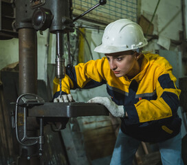 industrial worker wearing uniform safety helmet glove operate drill press machine in workshop worker intently focus on task ensure precision safety. background show various tool equipment industrial