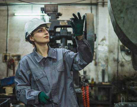 worker woman in uniform safety helmet operate machin industrial setting. worker focus on adjust tool and equipment showcasing precision and attention detail required in manufacturing environment. - Powered by Adobe